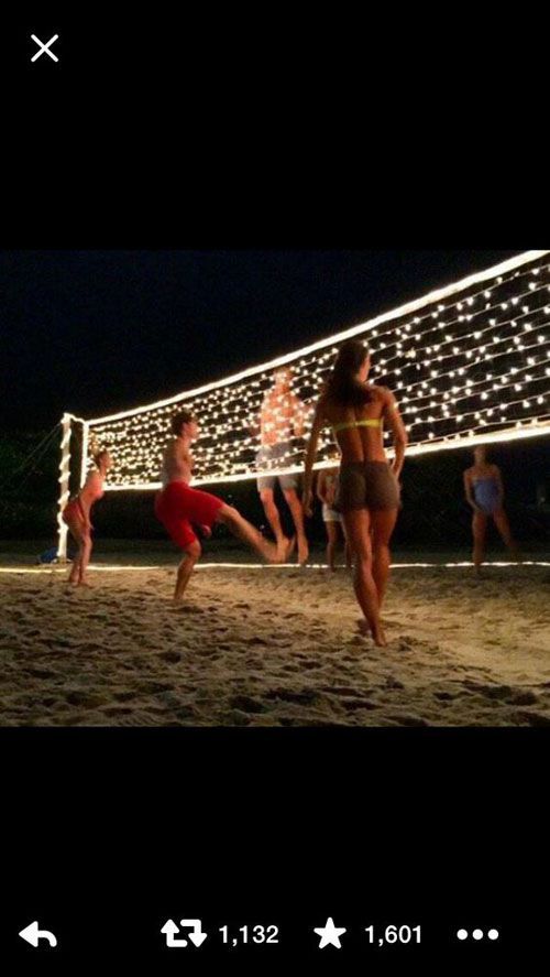 people are playing volleyball on the beach at night with lights strung across the sand and in front of them