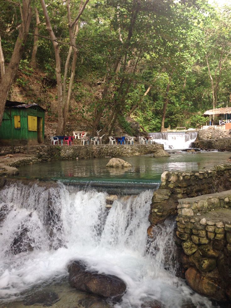 a small waterfall in the middle of a forest filled with trees and people sitting at tables