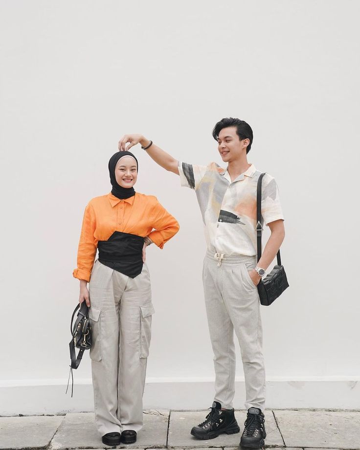 two people standing next to each other near a white wall and one is holding his arm up