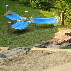 two blue hammocks sitting on top of a grass covered field next to rocks