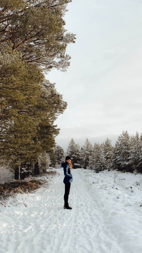 a person standing in the middle of a snow covered road taking a photo with their cell phone