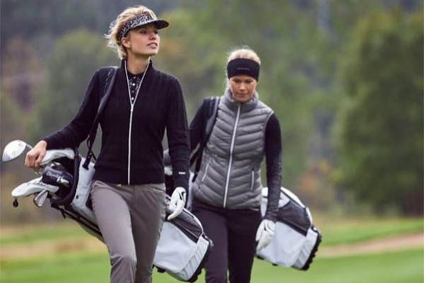 two women walking with golf bags on their back and one carrying a bag in her hand