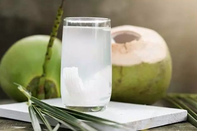 a glass of water sitting on top of a wooden table next to an open coconut