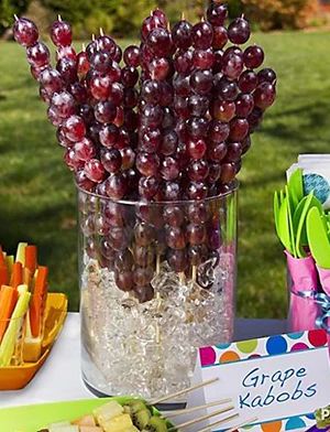 a bunch of grapes in a glass vase on a table next to other food items