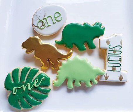 some cookies are on a white plate with green and yellow icing in the shape of dinosaurs