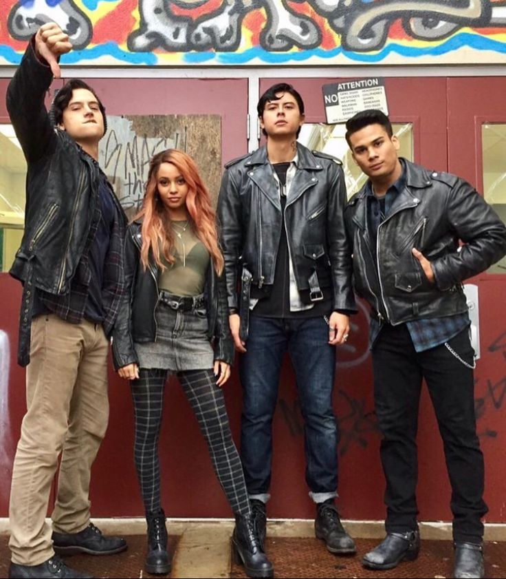 four people standing in front of a wall with graffiti on it and one person taking a selfie