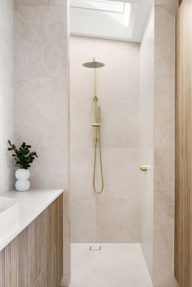 a walk in shower sitting next to a white sink and counter top under a skylight