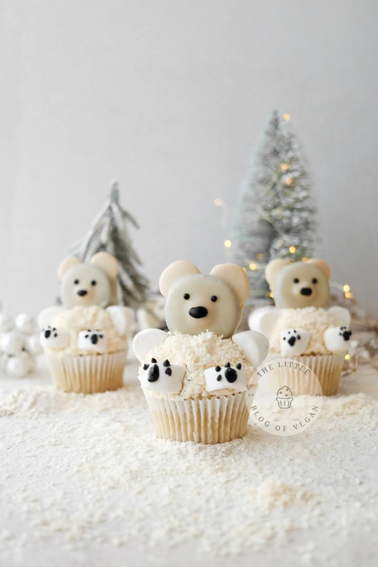 cupcakes decorated with white frosting and teddy bears on snow covered ground next to small christmas trees