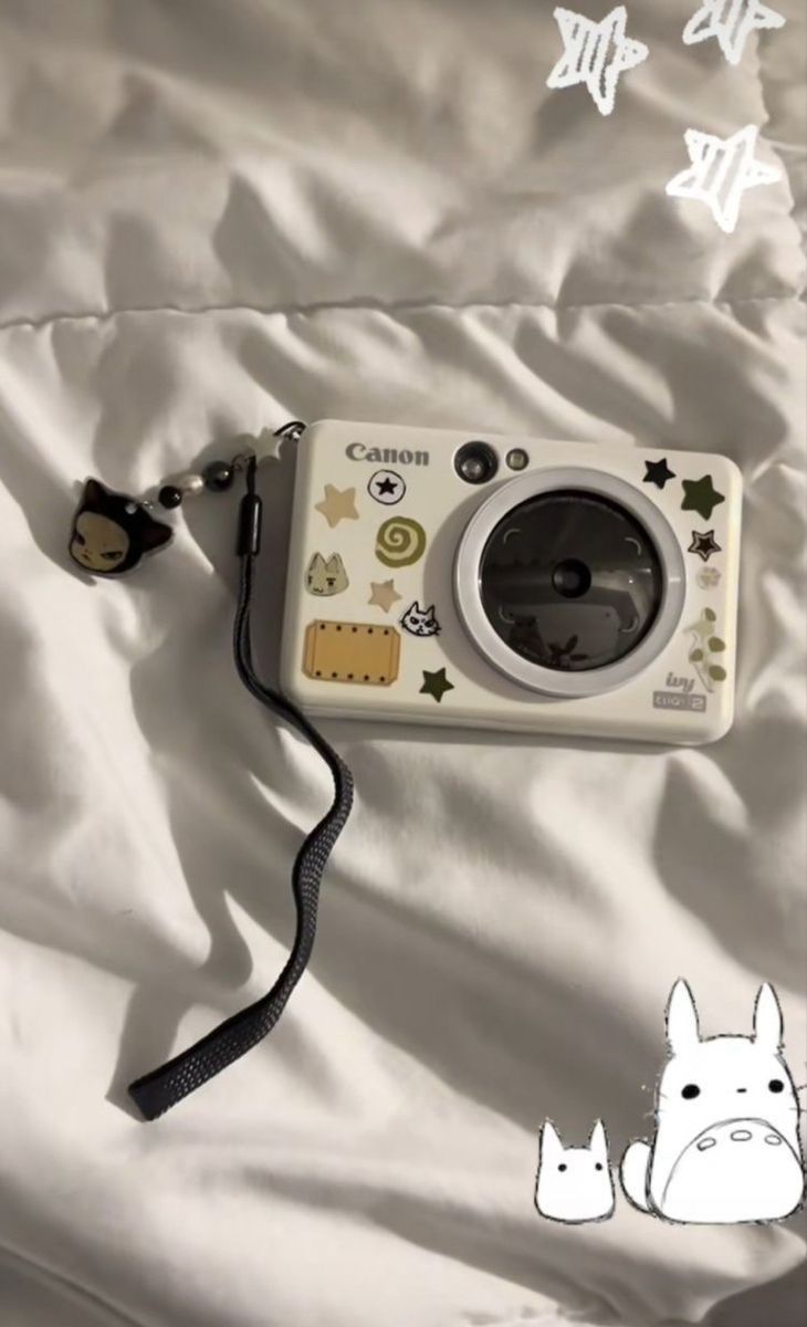 a camera is laying on a bed with white sheets and stars around it, along with an animal sticker