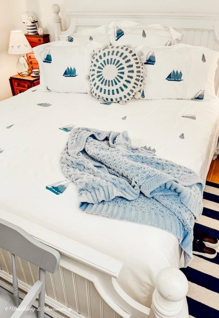 a white bed with blue and white decor on it's headboard, in a bedroom