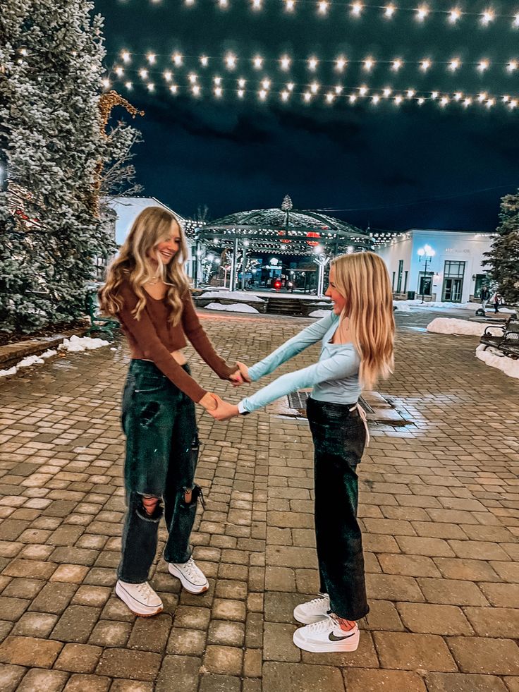 two young women holding hands in front of a building with christmas lights on the roof