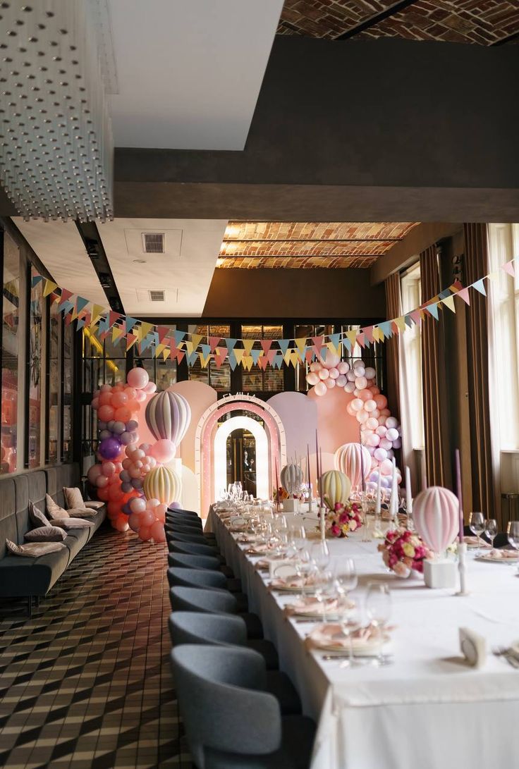 a long table set up for a party with balloons and streamers hanging from the ceiling