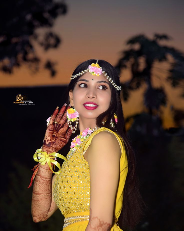 a woman in yellow dress holding her hand up to her face with the sun setting behind her