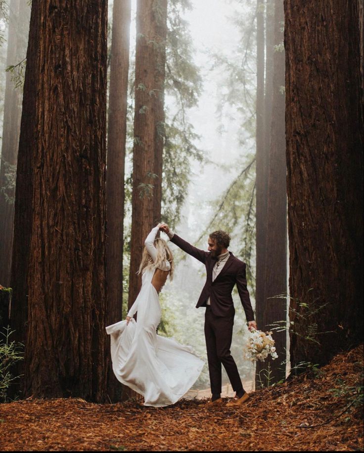 a bride and groom in the woods holding each other's hands as they walk through tall trees