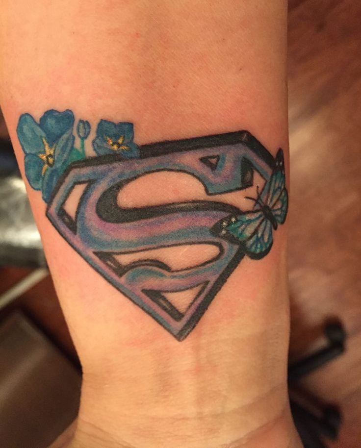 a superman tattoo on the ankle with blue flowers and a letter s in the center