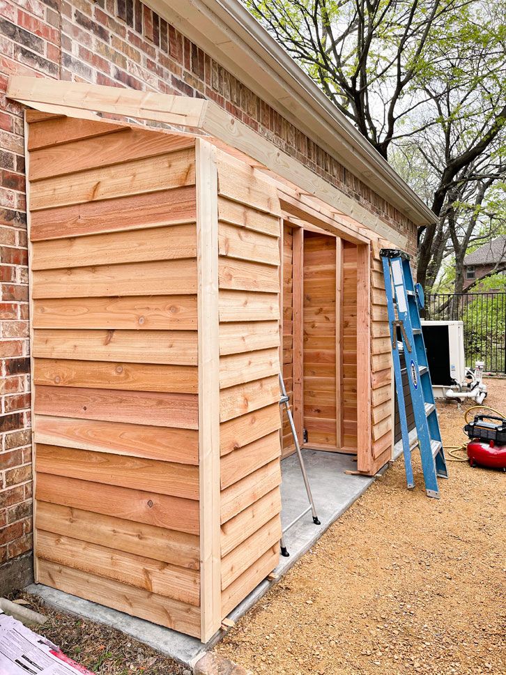 a small wooden shed is being built on the side of a brick building with ladders