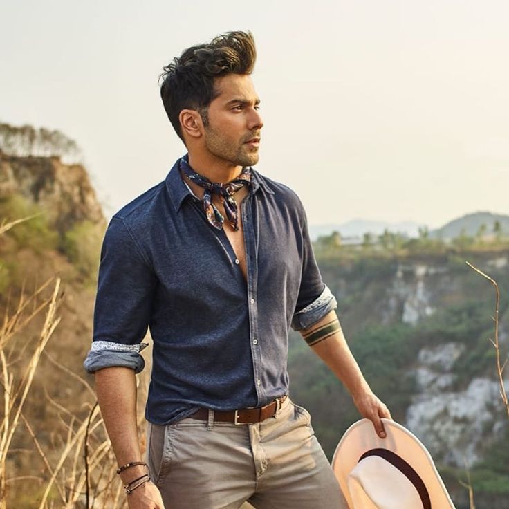 a man standing on top of a hill with a hat in his hand and looking off into the distance