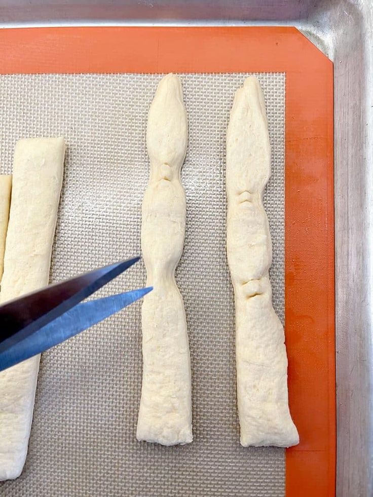 someone is cutting dough into long pieces on a baking sheet with a pair of scissors