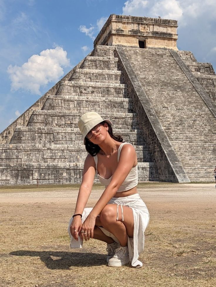 a woman kneeling down in front of an ancient pyramid with her hand on her knee