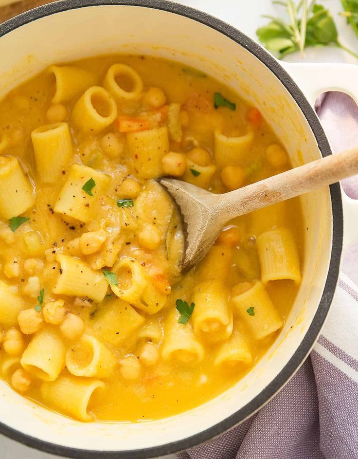 a wooden spoon in a pot filled with macaroni and cheese soup on top of a table