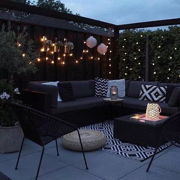 an outdoor living area with black furniture and string lights on the fence behind it at night