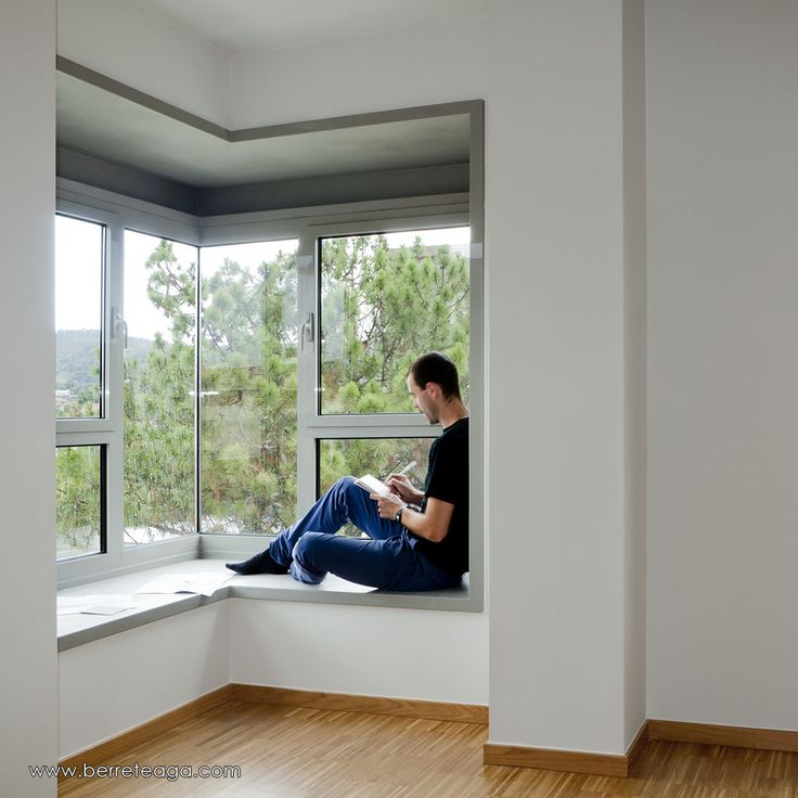 a man sitting on a window sill reading a book in front of a large window