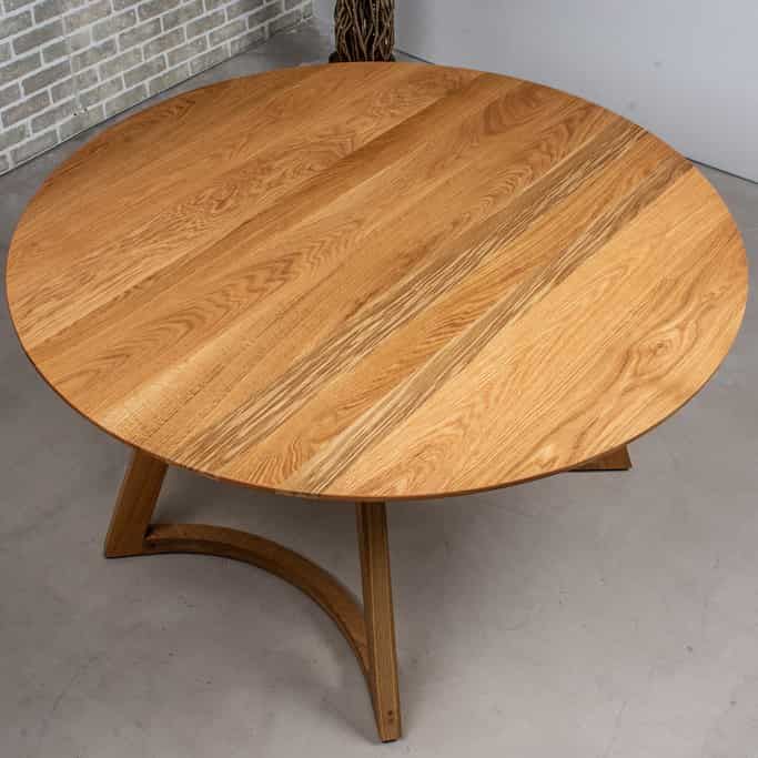 a round wooden table sitting on top of a cement floor next to a brick wall