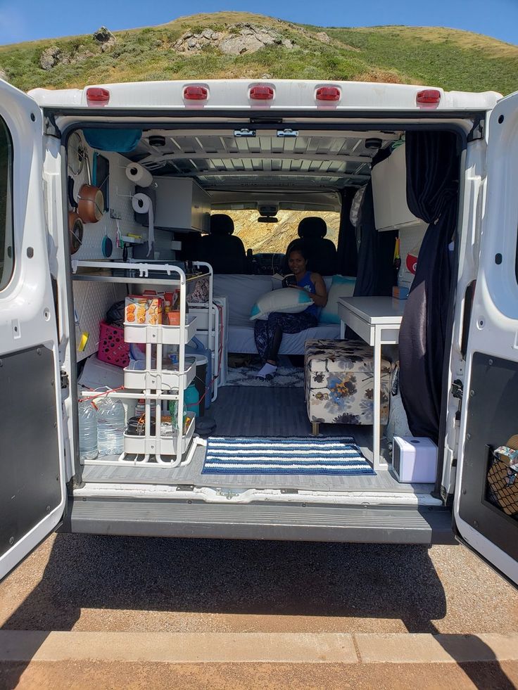 the back end of a van with its doors open and two people sitting in it