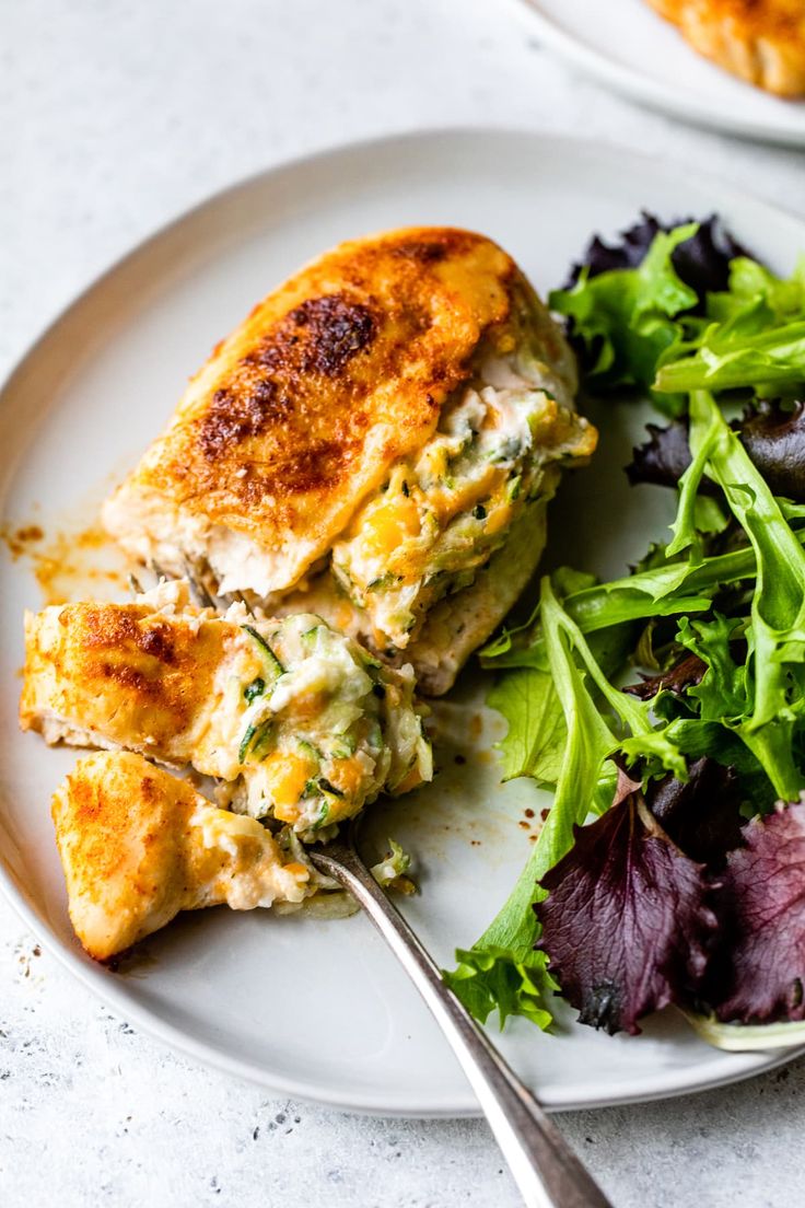 a white plate topped with chicken and salad next to a fork on a marble table