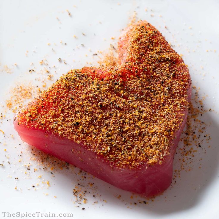 a piece of meat with seasoning on it sitting on a white plate in the shape of a heart