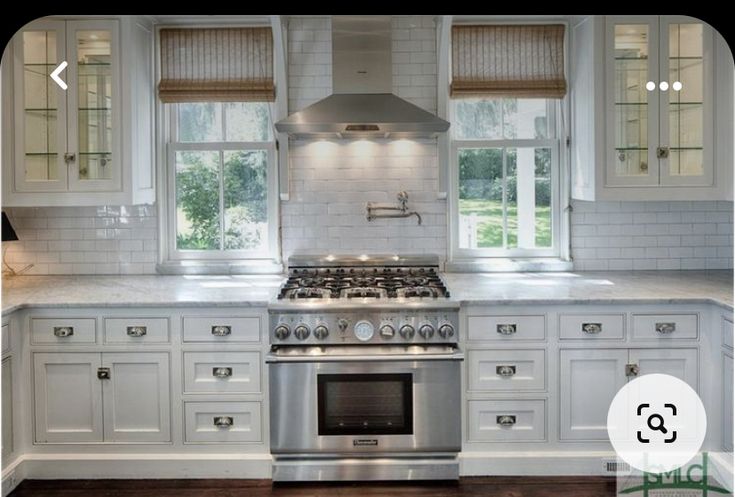 a kitchen with white cabinets and stainless steel stove top oven in front of two windows