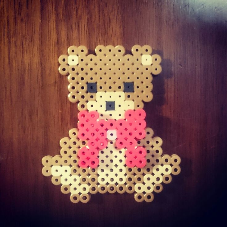 a teddy bear made out of perler beads on a wooden surface with a pink bow tie