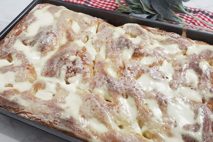 a pan filled with cinnamon rolls covered in icing next to a potted plant