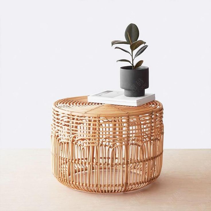 a plant is sitting on top of a wicker stool with a magazine in it