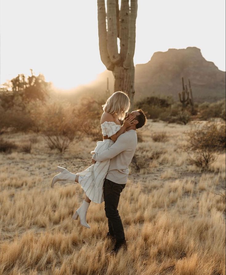 a man holding a woman in his arms while standing next to a saguado