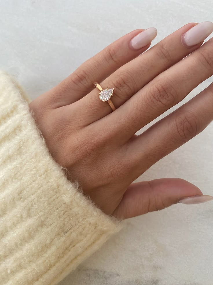 a woman's hand wearing a gold ring with a pear shaped diamond on it