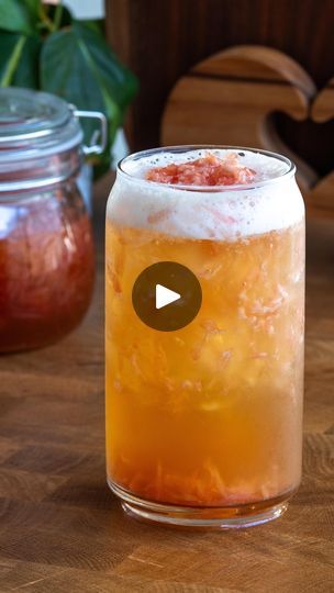 a glass filled with liquid sitting on top of a wooden table next to a jar