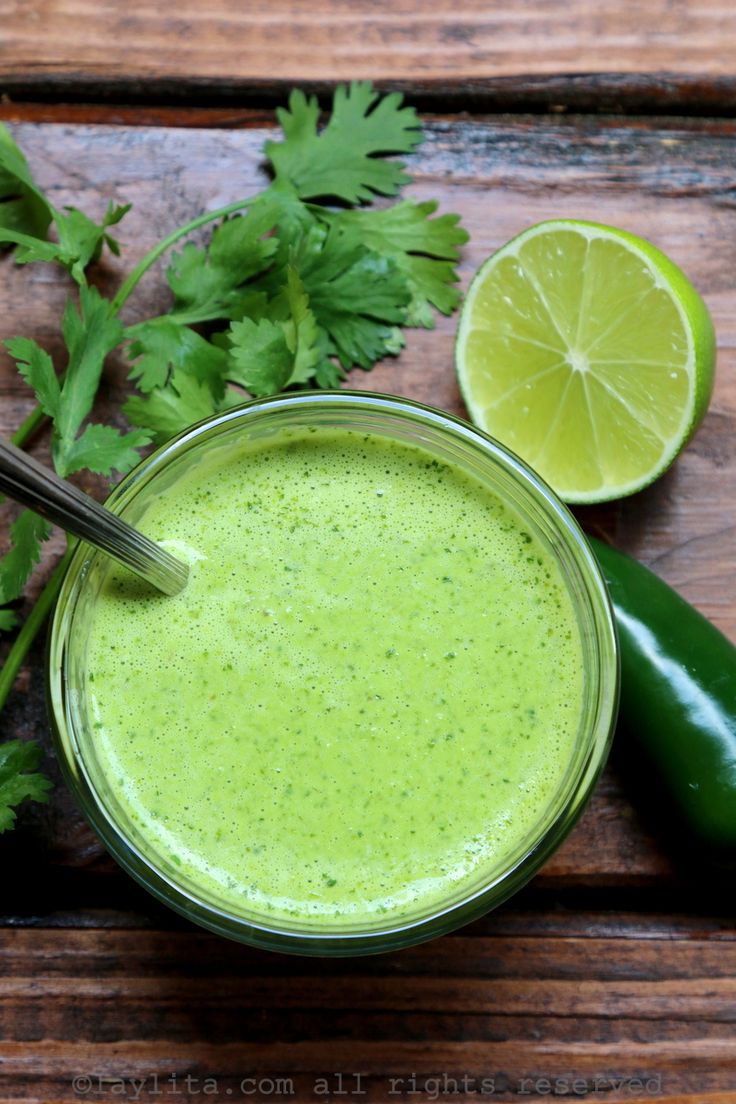 a green smoothie in a glass surrounded by cilantro and lime