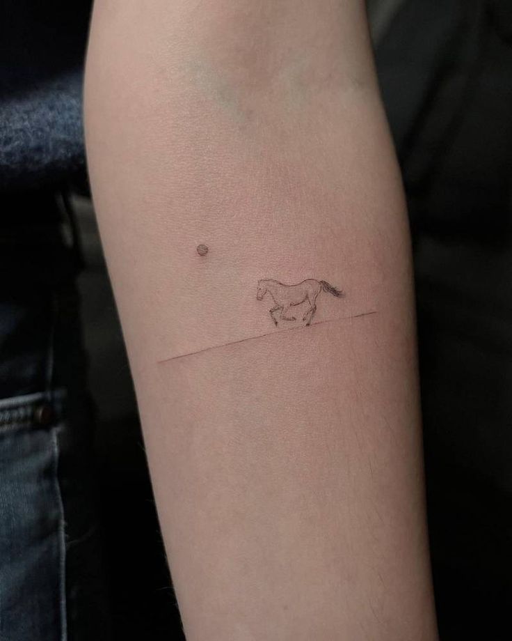 a person with a small tattoo on their arm that has a horse running in the distance