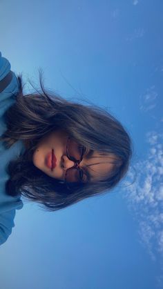 a woman with long hair and sunglasses standing in front of the camera, looking up into the sky