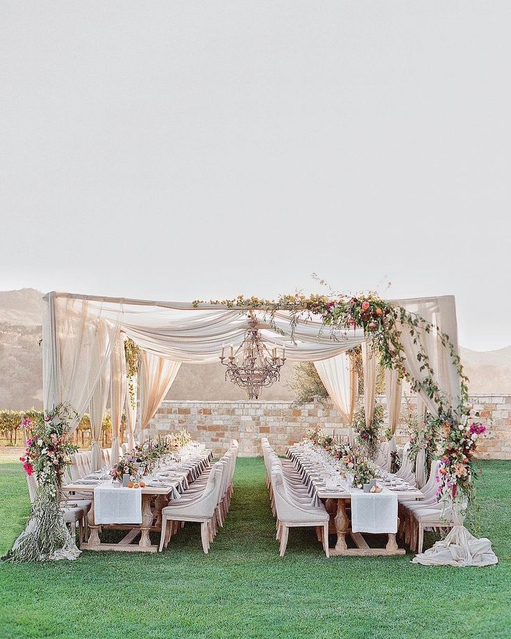 an outdoor wedding setup with white linens and greenery on the table, chandelier and chairs