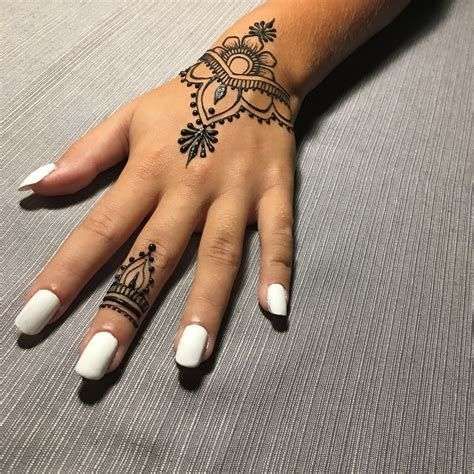 a woman's hand with a henna tattoo on her left wrist and white nails