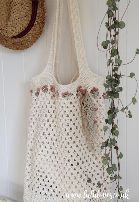 a white crocheted bag hanging on the wall next to a hat and plant