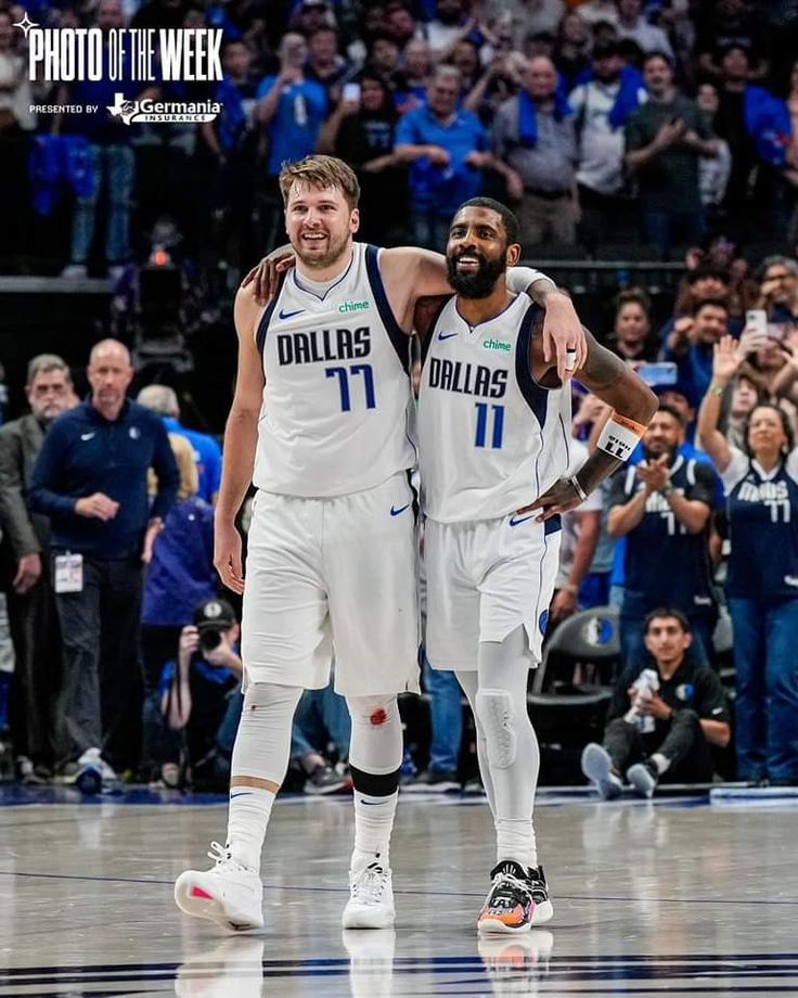 two men in white uniforms standing next to each other on a court with people watching