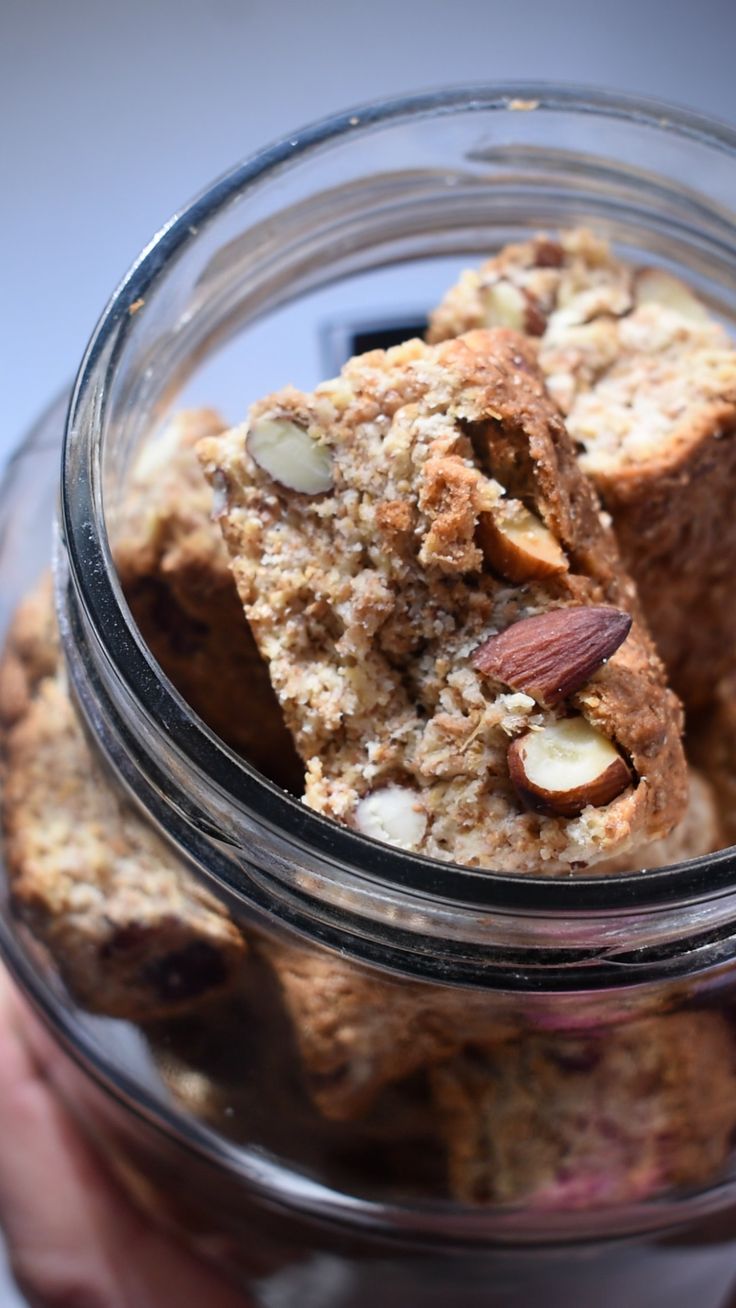 a person holding a glass jar filled with cookies and almonds on top of it