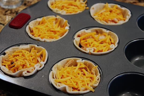 six mini pizzas with cheese on them sitting in a muffin tin ready to go into the oven