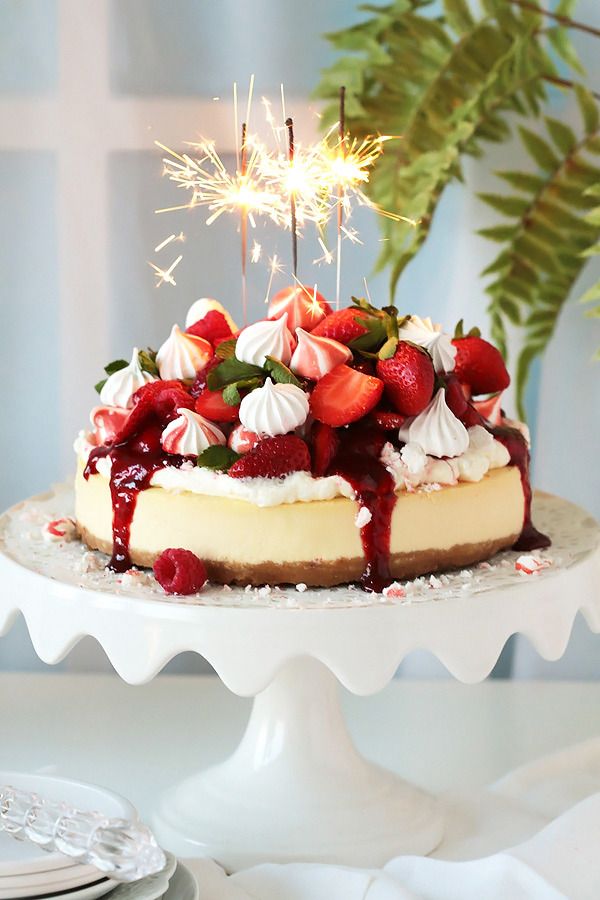 a cheesecake with strawberries and whipped cream is on a white cake platter