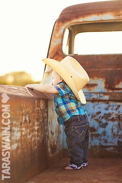 a little boy wearing a cowboy hat standing in the back of an old truck