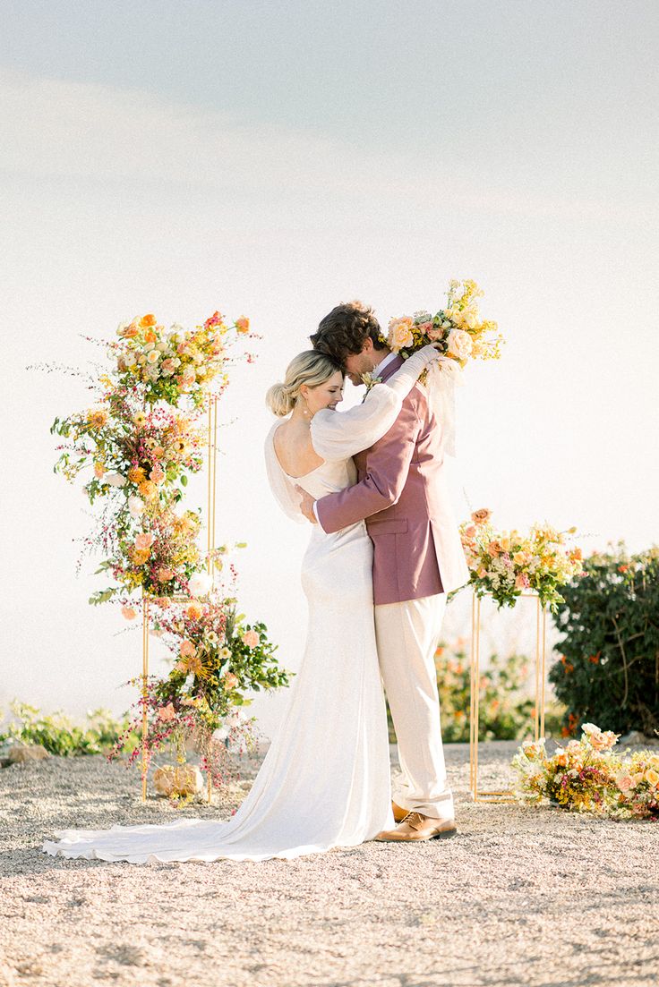 a bride and groom embracing each other in front of an arch with flowers on it