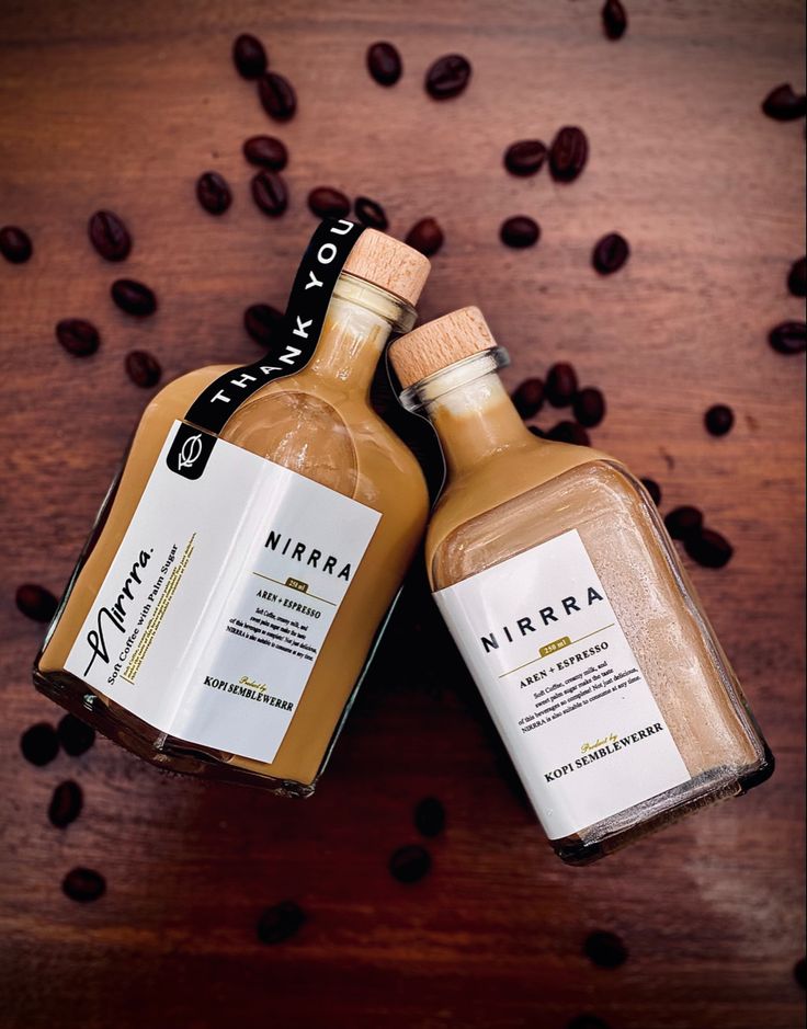 two bottles of coffee sitting on top of a wooden table next to some coffee beans